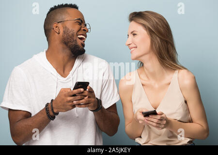 Happy multiethnic couple laugh using smartphones together Stock Photo