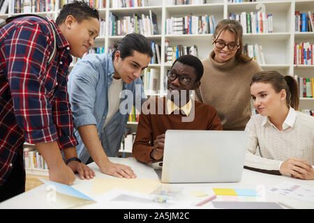 Multi-ethnic group of students studying together in college library, focus on African-American man using laptop, copy space Stock Photo