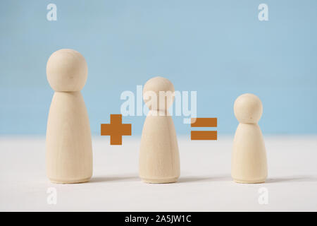 Wooden male, female and child figures with painted brown signs plus and equal on blue background. The concept of pregnancy planning. Stock Photo