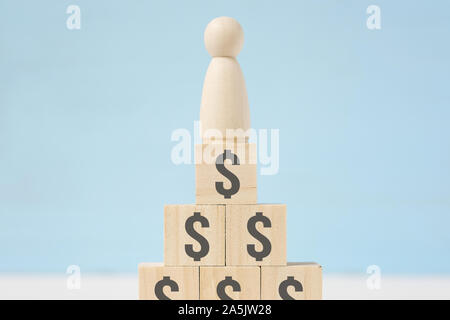 The abstract wooden figure of man on toy blocks with painted dollar signs on blue background. Concept of wealth. Stock Photo
