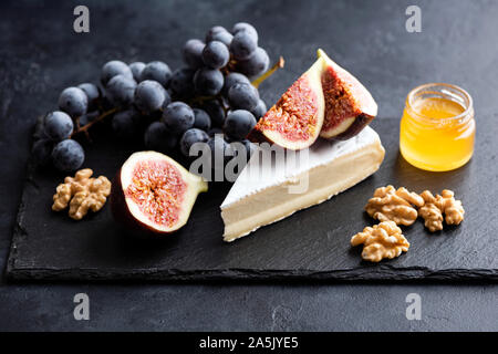 Brie or camembert cheese board with walnuts, grapes, figs and honey served on black slate plate. Gourmet appetizer Stock Photo