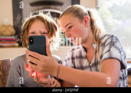Two children, a teenager and her 6 year old brother holding a smart phone, taking selfies. Stock Photo