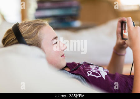 13 year old girl at home wearing headphones and looking at smart phone Stock Photo
