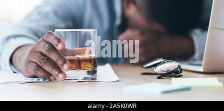 Drunk black employee sleeping at workplace, holding glass with alcohol Stock Photo
