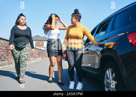 Young woman and two teenage sisters opening car door, UK Stock Photo