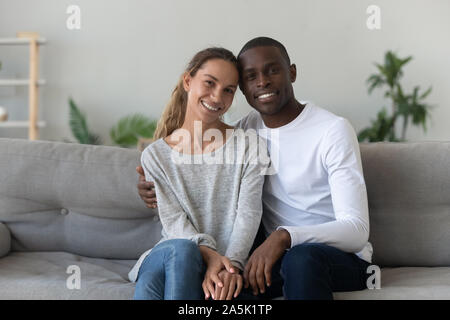 Portrait of smiling multiracial couple sit on couch at home Stock Photo