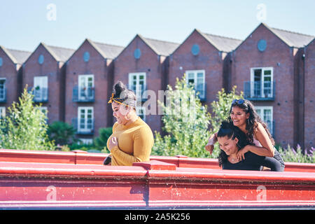 Young woman getting piggy back from teenage sister crossing footbridge Stock Photo