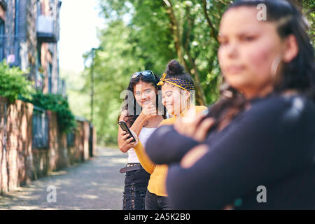 Young woman with teenage sisters looking at smartphone by park Stock Photo