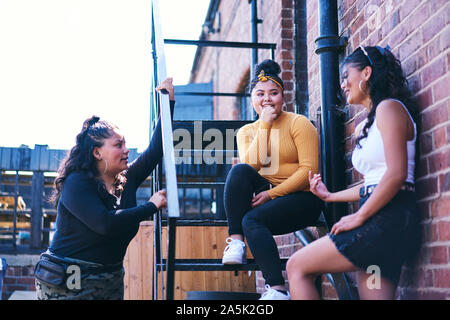 Young woman and her teenage sisters chatting on fire escape Stock Photo