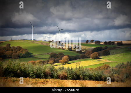 Wind turbines on crest of hill above fertile valley with dramatic sky Stock Photo