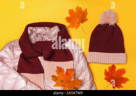 Top view of the composition of warm childrens clothing and autumn leaves on a yellow background. Stock Photo