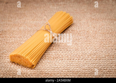 Italian spaghetti pasta tied in bunch by craft rope lying on natural surface Stock Photo