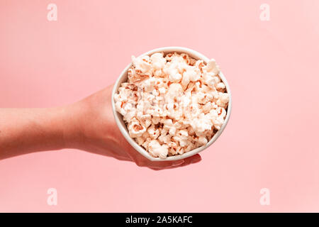 Food composition of hand holding popcorn in bucket on pink background top view copy space Stock Photo
