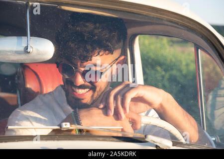 Handsome and flirtatious gay boy driving a car in summer. Stock Photo