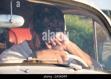 Handsome and flirtatious gay boy driving a car in summer. Stock Photo