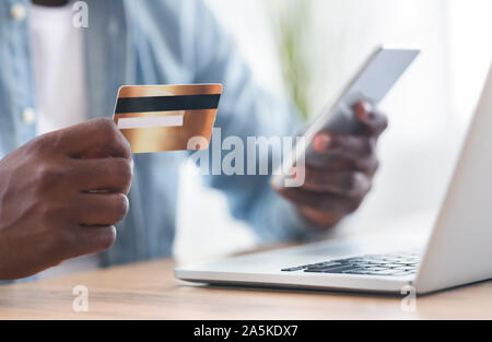 Black man using card and smartphone for paying bills online Stock Photo