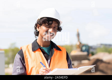 Male engineer on construction site writing in notebook, head and shoulder portrait Stock Photo