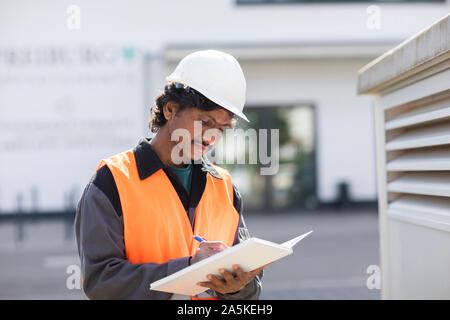 Male engineer outside industrial building writing in notebook Stock Photo
