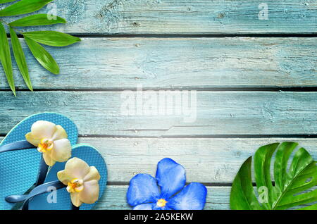 Summer flat lay background. Tropical palm leaves, flip flops and flower on old blue wooden background. Stock Photo