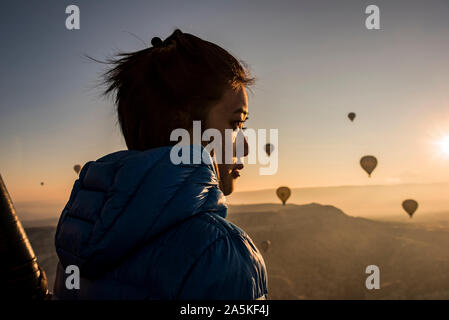Woman enjoying view, hot air balloons flying in background, Göreme, Cappadocia, Nevsehir, Turkey Stock Photo