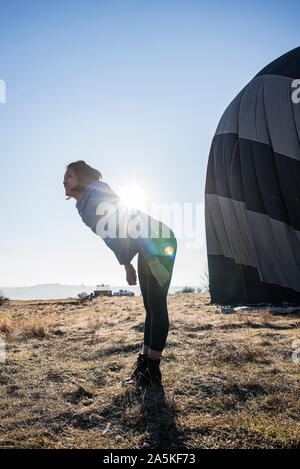 Woman bending forward against sunlight, hot air balloon in background, Göreme, Cappadocia, Nevsehir, Turkey Stock Photo