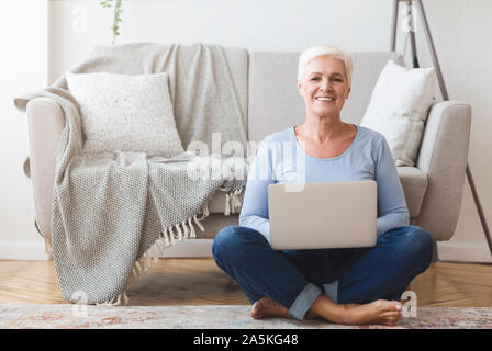 Active old woman sitting on floor and using laptop Stock Photo