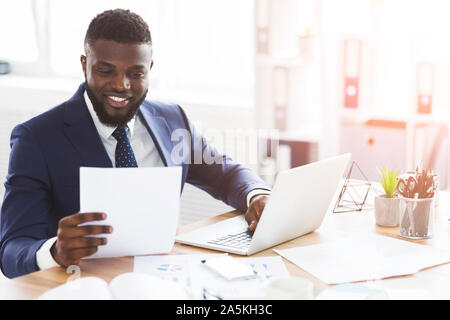 Satisfied black businessman checking documents, sitting in modern office Stock Photo
