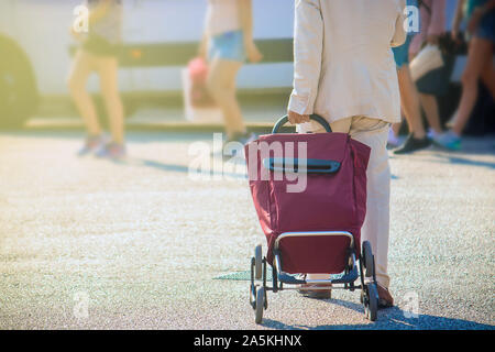 walking away with a trolley. Detail of red suitcase and defocused people on the background (copy space on the left) Stock Photo