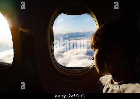 Teenage boy looking out through airplane window at clouds on airplane journey Stock Photo