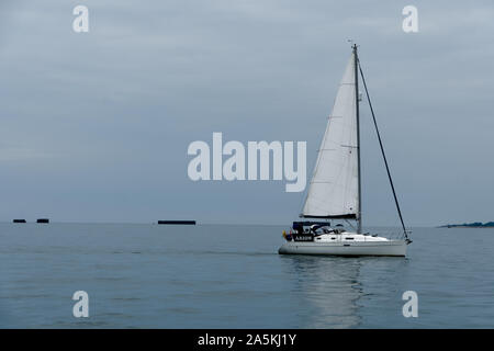 Yacht motorsailing in Mulberry Harbour at Arromanches, Normandy, France. Stock Photo