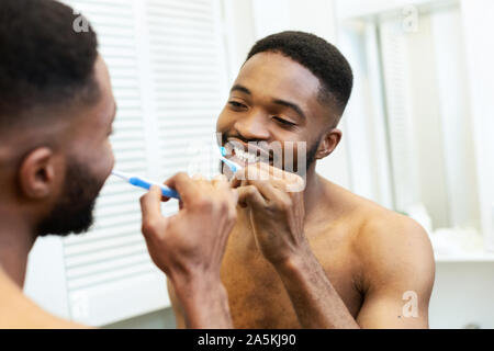 Millennial black guy brushing his teeth in bathroom Stock Photo