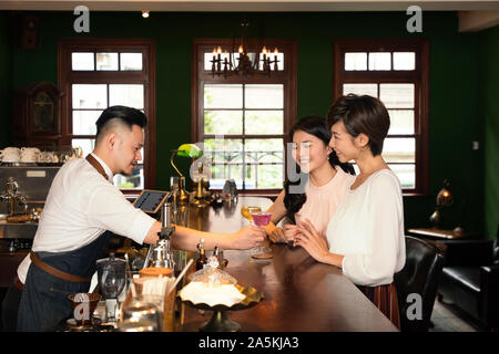 Bartender serving cocktails to two young women at bar Stock Photo