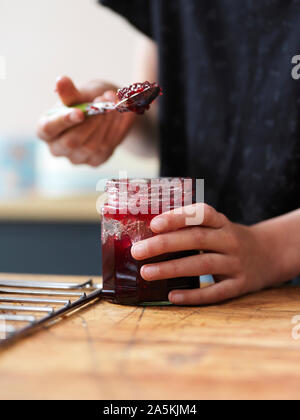 Girl baking a cake, holding spoonful of jam at kitchen table, close up of hands Stock Photo