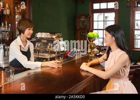 Female bartender serving drink to woman at bar counter Stock Photo