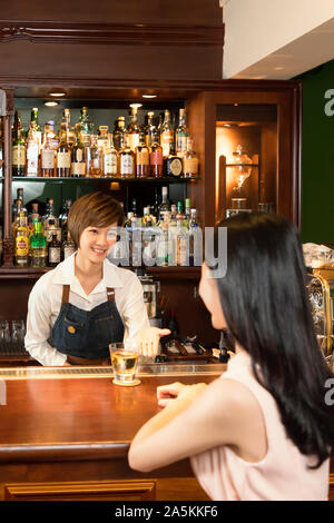 Female bartender serving drink to woman at bar counter Stock Photo