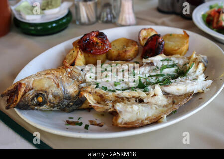 Dinner in Cyprus including grilled sea bass (entire fish), potatoes and grilled veggies like tomatoes. Healthy and delicious Mediterranean style dish. Stock Photo