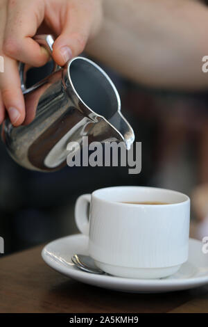 Pouring milk / cream from a silver metal can into a fresh cup of morning coffee. Wonderful way to start a day! The coffee is full of energy! Stock Photo