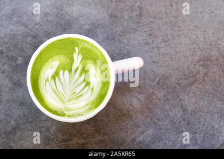 Vegan green tea matcha with oat milk with latte art in white cup on concrete table. Top view, with place for text. Stock Photo