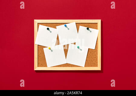 Cork board with wooden frame with five pinned blank notes on red background, view from above with place for text. Stock Photo