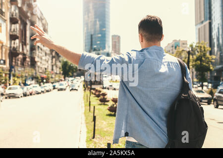 Outdoors Leisure. Stylish guy traveler standing near road hitchhiking back view Stock Photo