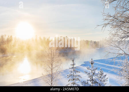 Mist over freezing river on a sunny cold winter day. Trees covered with frost and snow. Stock Photo
