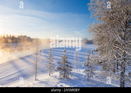 Mist over freezing river on a sunny cold winter day. Trees covered with frost and snow. Stock Photo