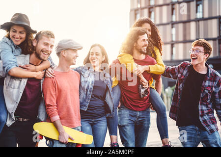 Group of young people having fun in the city center - Happy friends piggybacking while laughing and walking together outdoor Stock Photo