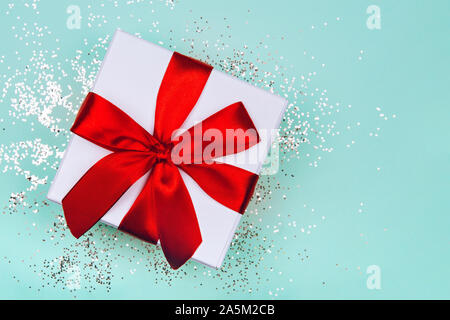 Gift box with red bow on green mint background with delicate golden sparkles. Stock Photo