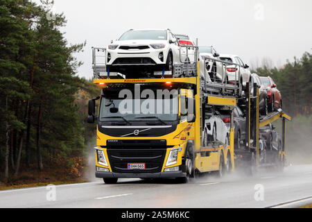 Yellow Volvo FM vehicle carrier of Kuljetus J. Olli Oy transports a load of new cars on wet highway in autumn. Tenhola, Finland. October 18, 2019. Stock Photo