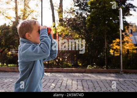 young boy stood in a street looking through binoculars Stock Photo