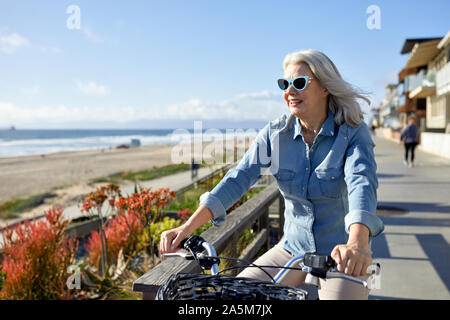 Smiling senior woman wearing sunglasses riding bicycle on road at Manhattan Beach in city Stock Photo