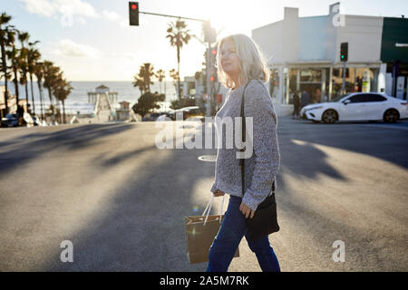 Side view of senior woman with shopping bag walking on road in city during sunset Stock Photo