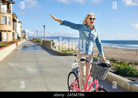 Cheerful senior woman wearing sunglasses riding bicycle on road against sky in city Stock Photo