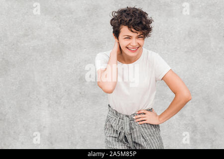 Charming young woman with creative hairstyle is smiling and posing with joyful embarrassed face. Emotions and feelings. Stock Photo